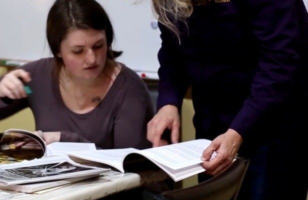 A staff member and a resident at a table, working through a printed workbook.