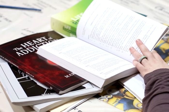 An open copy of The Heart of Addiction and other Worthy Women curriculum books on a table, a hand resting on the page.