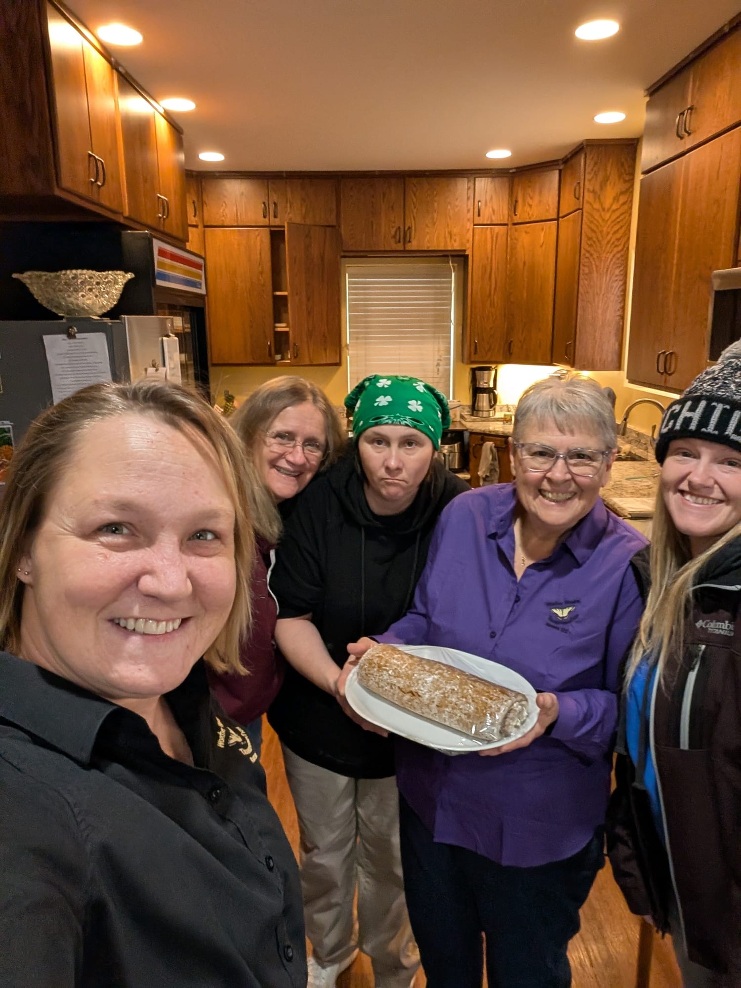 Five women together in the kitchen, one holding a fresh-baked roll.