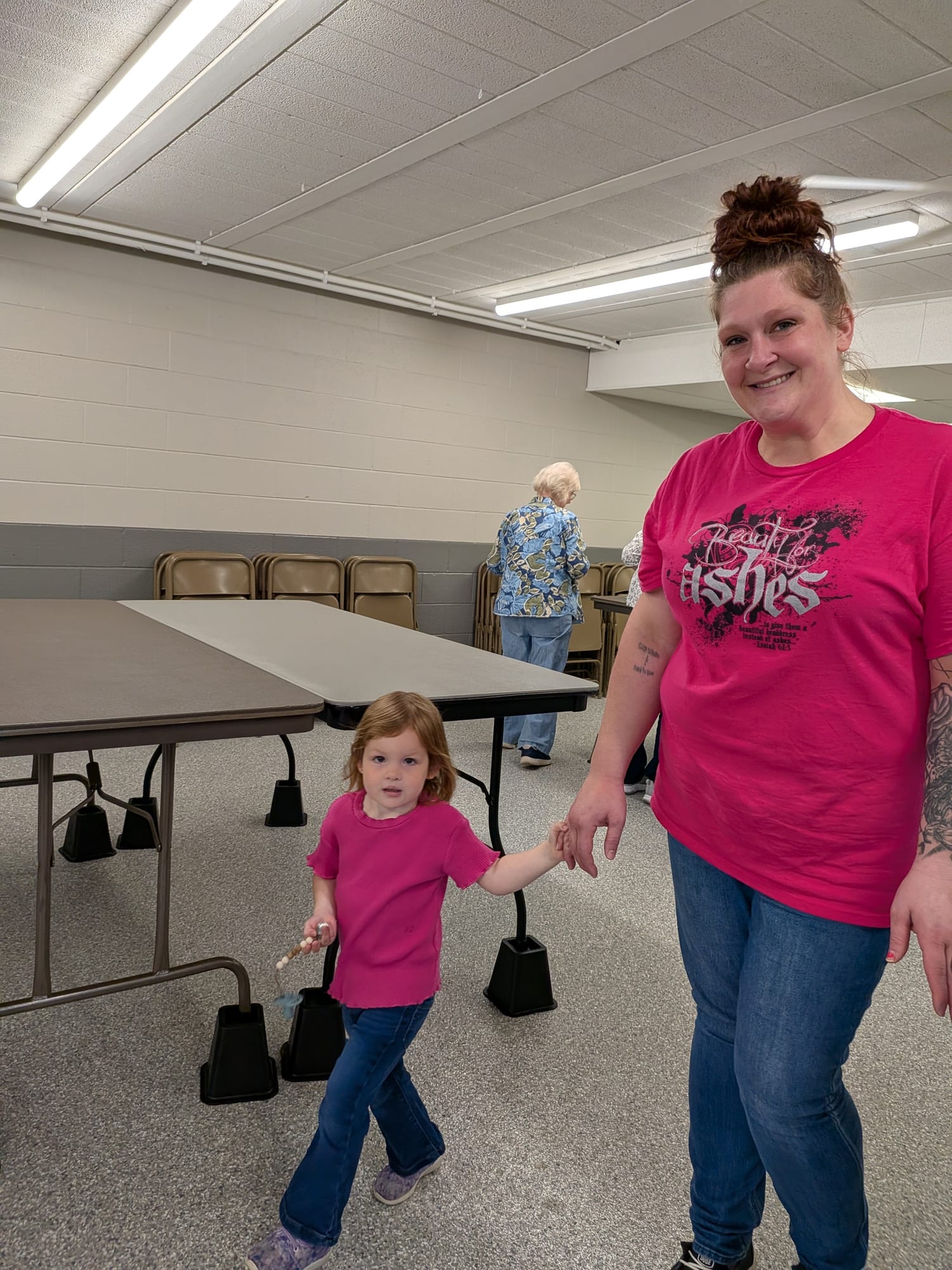 A smiling woman holding hands with her young daughter in a church hall.